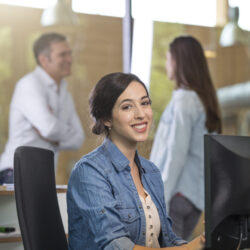 Portrait of business woman at desk with communicating colleagues in the background