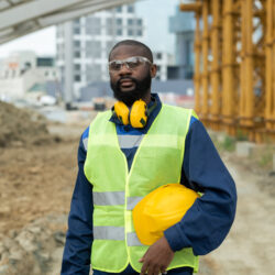 African young male builder in uniform standing on construction site