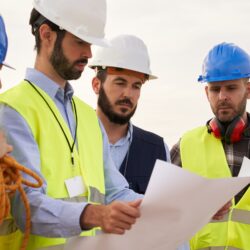 Group of Caucasian engineers check a plan at an air turbine field. Ecology, energy and industrial aspects are studied by the four. Environment and renewable energies are into the minds of these people